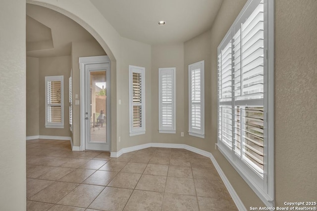 entrance foyer featuring light tile patterned flooring, arched walkways, and baseboards