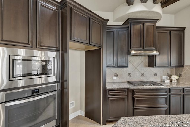 kitchen with light stone counters, dark brown cabinetry, stainless steel appliances, and backsplash