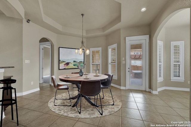 dining room with arched walkways, a raised ceiling, and light tile patterned flooring
