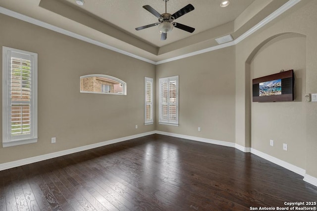 empty room featuring ornamental molding, baseboards, dark wood-type flooring, a raised ceiling, and a ceiling fan