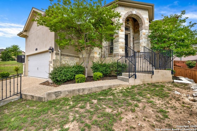 view of front of property with fence, stucco siding, an attached garage, and stone siding