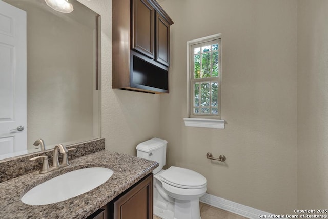 half bath with toilet, baseboards, and vanity