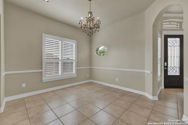 tiled foyer featuring an inviting chandelier, arched walkways, and baseboards