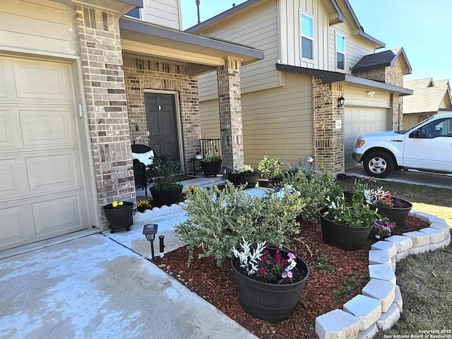 entrance to property featuring a porch, brick siding, an attached garage, and driveway