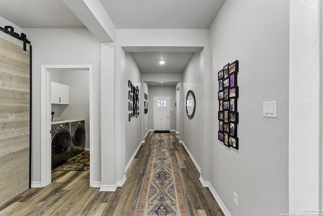 hallway featuring baseboards, dark wood-type flooring, a barn door, and washer and clothes dryer