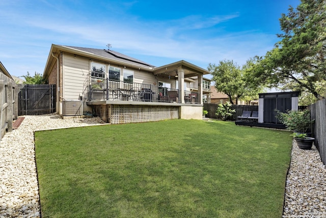 rear view of house with a fenced backyard, a wooden deck, a yard, and solar panels