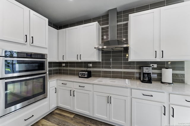 kitchen with wall chimney range hood, white cabinets, white electric cooktop, and double oven