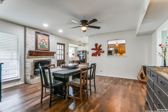 dining space with a brick fireplace, dark wood-style flooring, ceiling fan, and baseboards