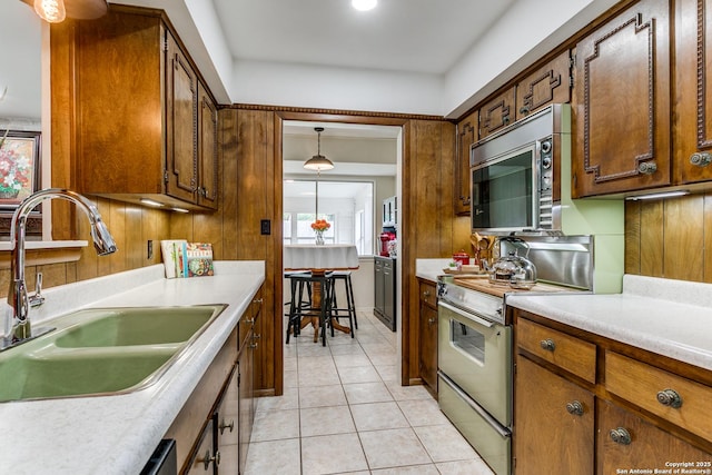 kitchen with a sink, light countertops, stainless steel microwave, electric stove, and light tile patterned floors