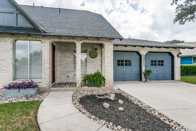property entrance featuring brick siding, driveway, roof with shingles, and a garage