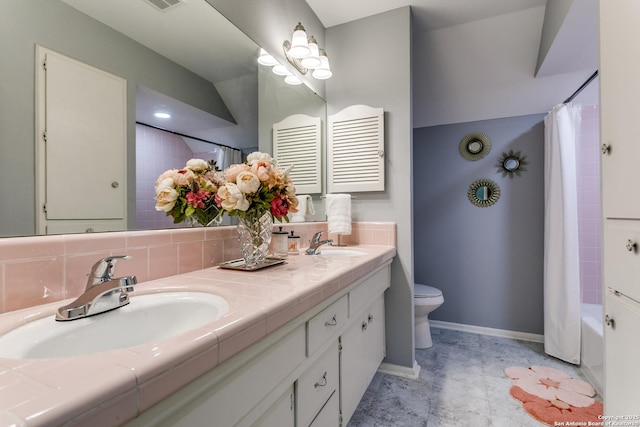 bathroom with double vanity, toilet, baseboards, and a sink