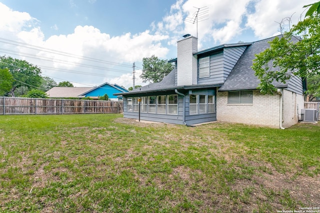 rear view of property featuring a chimney, central AC unit, brick siding, fence, and a yard