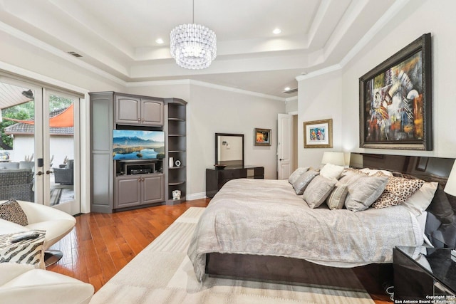 bedroom featuring a raised ceiling, access to exterior, wood finished floors, and a chandelier
