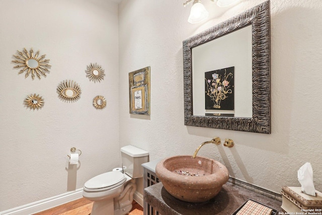 half bath with baseboards, vanity, toilet, and wood finished floors