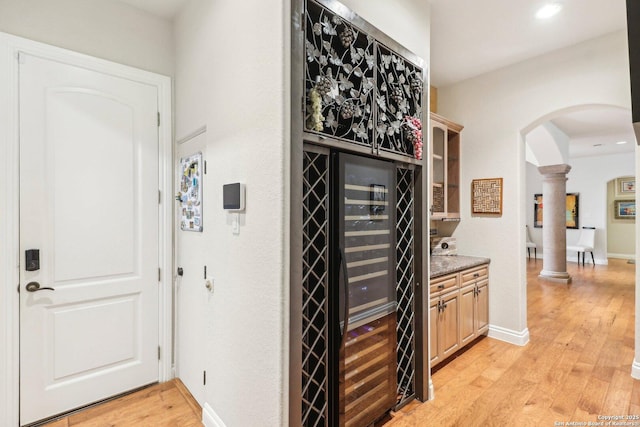 wine room with decorative columns, arched walkways, baseboards, light wood finished floors, and beverage cooler