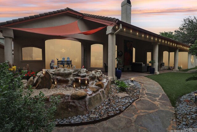 back of house at dusk featuring outdoor lounge area, a patio, stucco siding, a chimney, and a tile roof