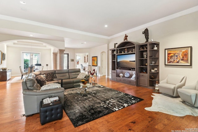 living room featuring crown molding, arched walkways, decorative columns, and wood finished floors