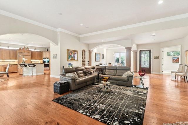living room featuring arched walkways, recessed lighting, light wood-type flooring, ornate columns, and ornamental molding