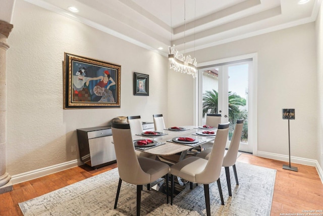 dining area featuring ornamental molding, baseboards, light wood-type flooring, a raised ceiling, and a chandelier