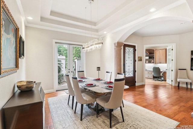 dining area featuring french doors, arched walkways, baseboards, a raised ceiling, and light wood finished floors