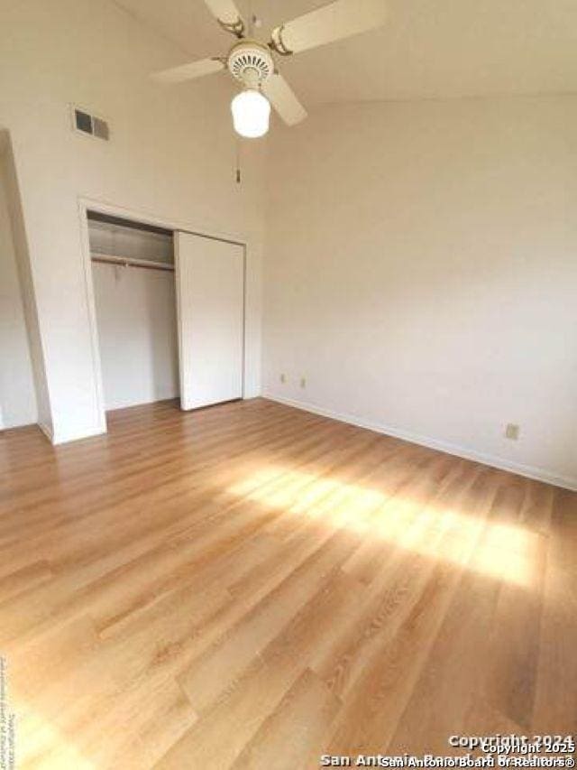 unfurnished bedroom with light wood finished floors, high vaulted ceiling, baseboards, visible vents, and a closet