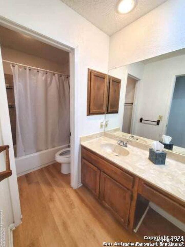 bathroom featuring vanity, shower / tub combo with curtain, wood finished floors, toilet, and a textured ceiling