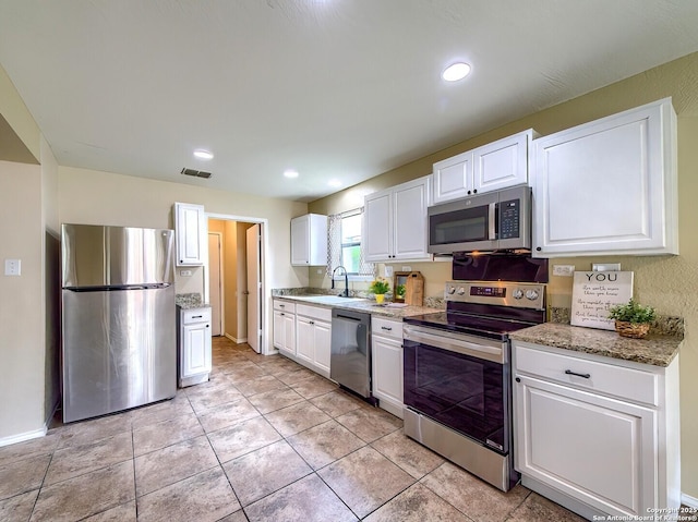 kitchen featuring white cabinets, appliances with stainless steel finishes, light stone counters, a sink, and visible vents