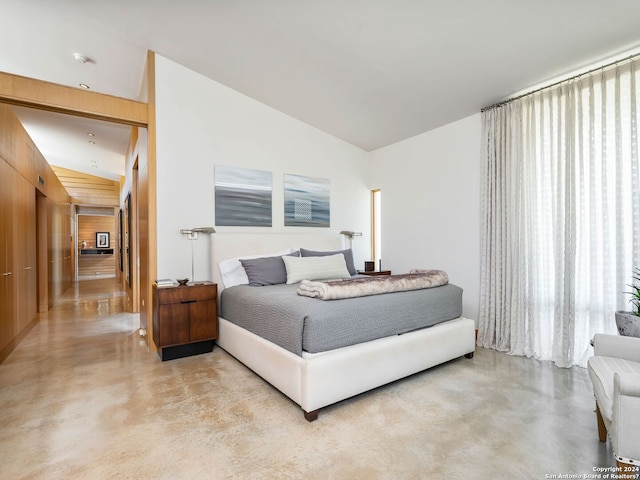 bedroom with vaulted ceiling, multiple windows, and concrete flooring