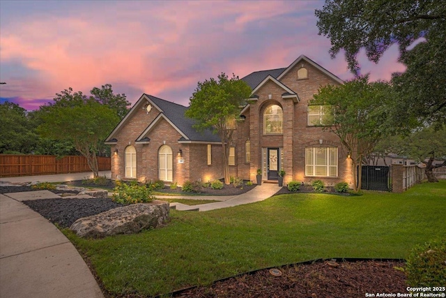 traditional-style home featuring brick siding, a gate, a front lawn, and fence