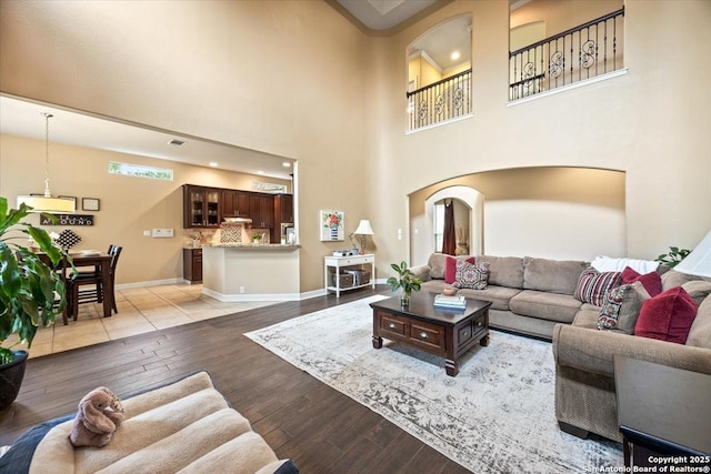 living room with a towering ceiling, light wood-style floors, baseboards, recessed lighting, and arched walkways