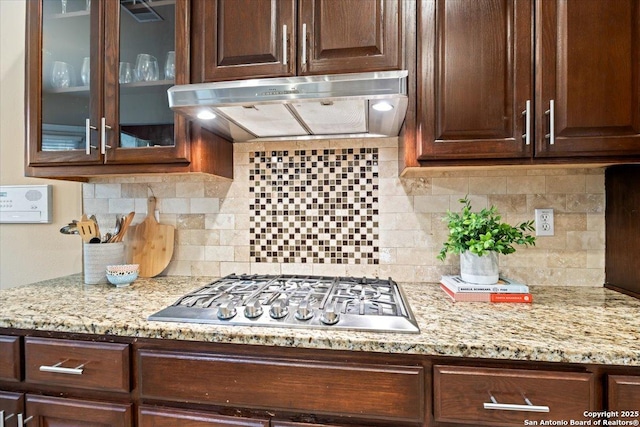 kitchen with glass insert cabinets, under cabinet range hood, dark brown cabinetry, and stainless steel gas stovetop