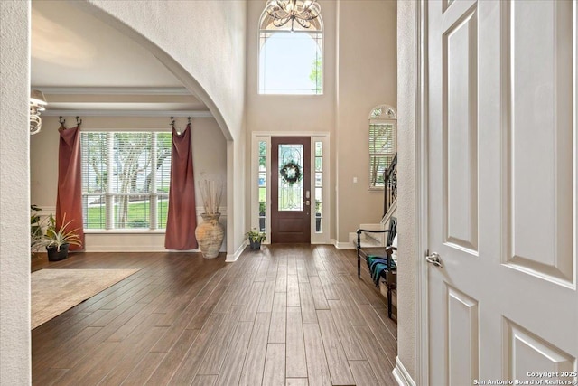 entrance foyer featuring crown molding, arched walkways, wood finished floors, baseboards, and a notable chandelier