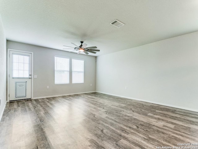 unfurnished room featuring a ceiling fan, baseboards, visible vents, and wood finished floors