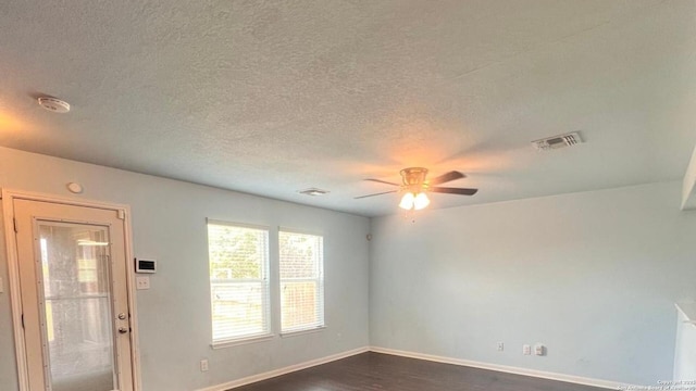 spare room with a textured ceiling, a ceiling fan, baseboards, visible vents, and dark wood-style floors