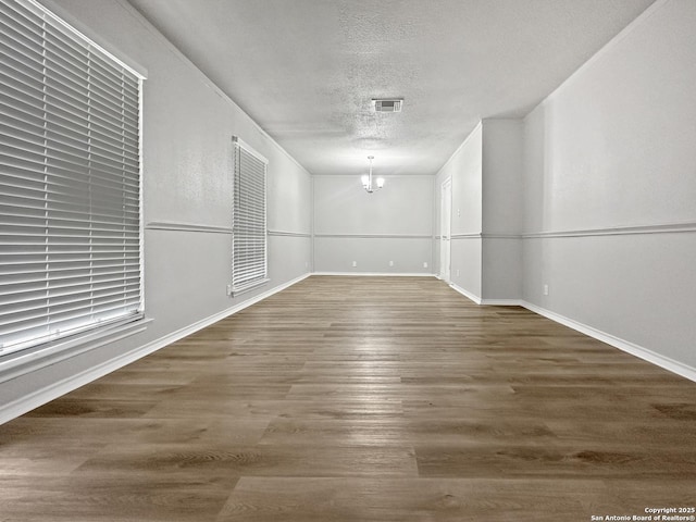 unfurnished room featuring baseboards, a textured ceiling, visible vents, and wood finished floors