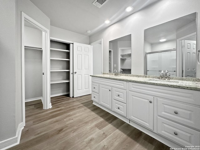 bathroom with a sink, a stall shower, wood finished floors, and visible vents