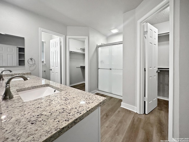 bathroom featuring a sink, a stall shower, wood finished floors, and a spacious closet