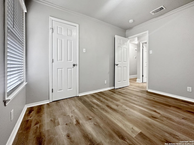 unfurnished bedroom with baseboards, visible vents, ornamental molding, and wood finished floors