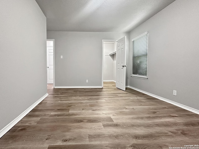 unfurnished bedroom with baseboards, wood finished floors, and a spacious closet