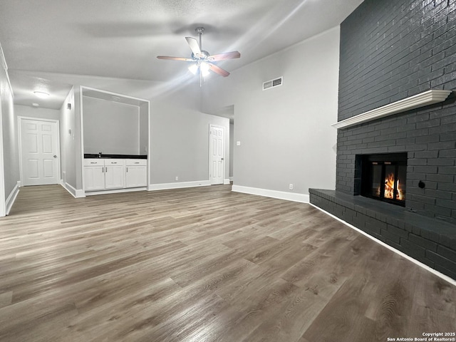 unfurnished living room featuring a ceiling fan, visible vents, a fireplace, baseboards, and light wood finished floors