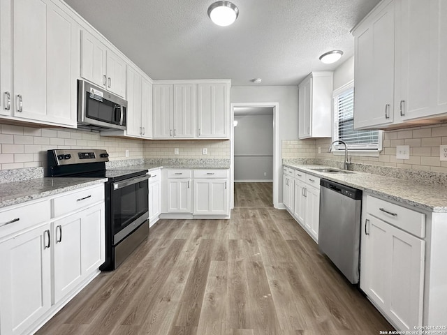 kitchen with a textured ceiling, white cabinets, a sink, light wood-style flooring, and appliances with stainless steel finishes