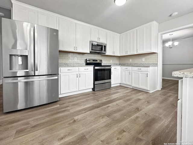 kitchen featuring decorative backsplash, light wood-type flooring, white cabinets, an inviting chandelier, and stainless steel appliances