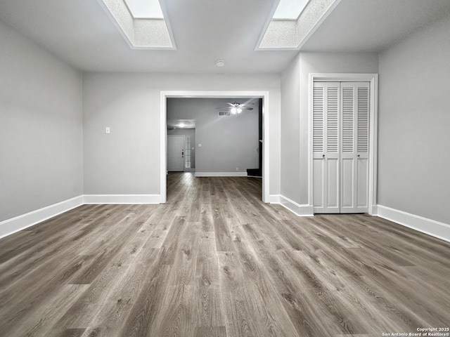 interior space featuring baseboards, a skylight, and wood finished floors