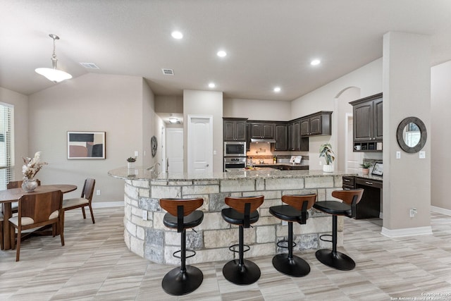 kitchen featuring vaulted ceiling, a large island with sink, dark brown cabinets, baseboards, and stainless steel appliances