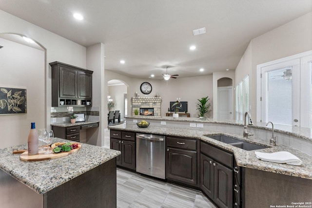 kitchen with dark brown cabinetry, ceiling fan, arched walkways, a sink, and dishwasher