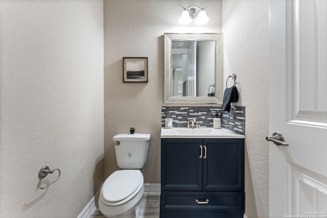 bathroom featuring vanity, a textured wall, backsplash, and toilet