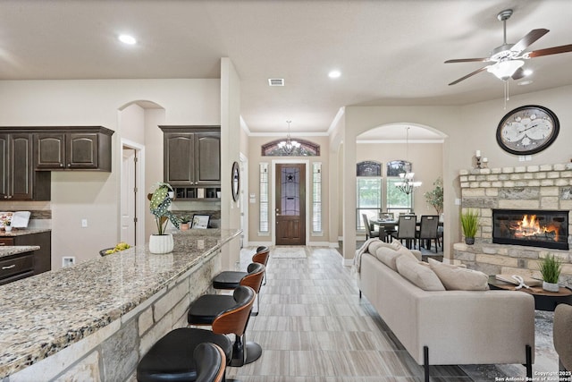 living room featuring visible vents, arched walkways, a fireplace, ceiling fan with notable chandelier, and recessed lighting