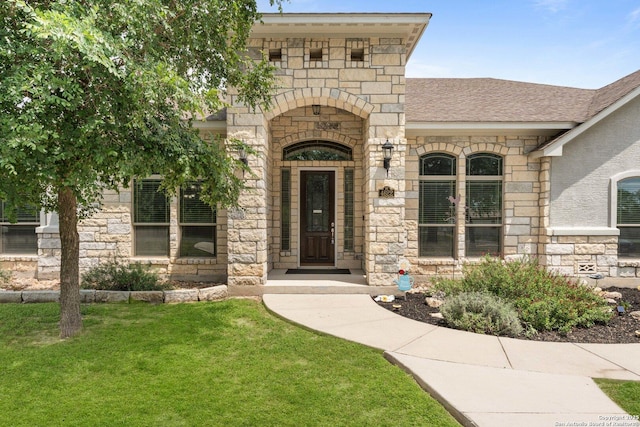 view of exterior entry with a shingled roof, a yard, and stone siding