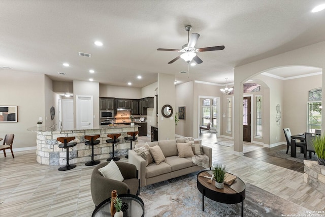 living room with crown molding, arched walkways, ceiling fan with notable chandelier, baseboards, and visible vents