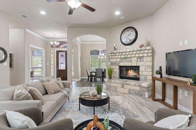 living room featuring a stone fireplace, visible vents, arched walkways, baseboards, and ceiling fan with notable chandelier